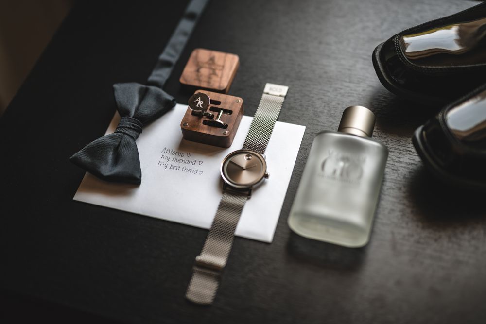 Flat lay of groom's accessories including watch, tie, and cufflinks on dark surface.
