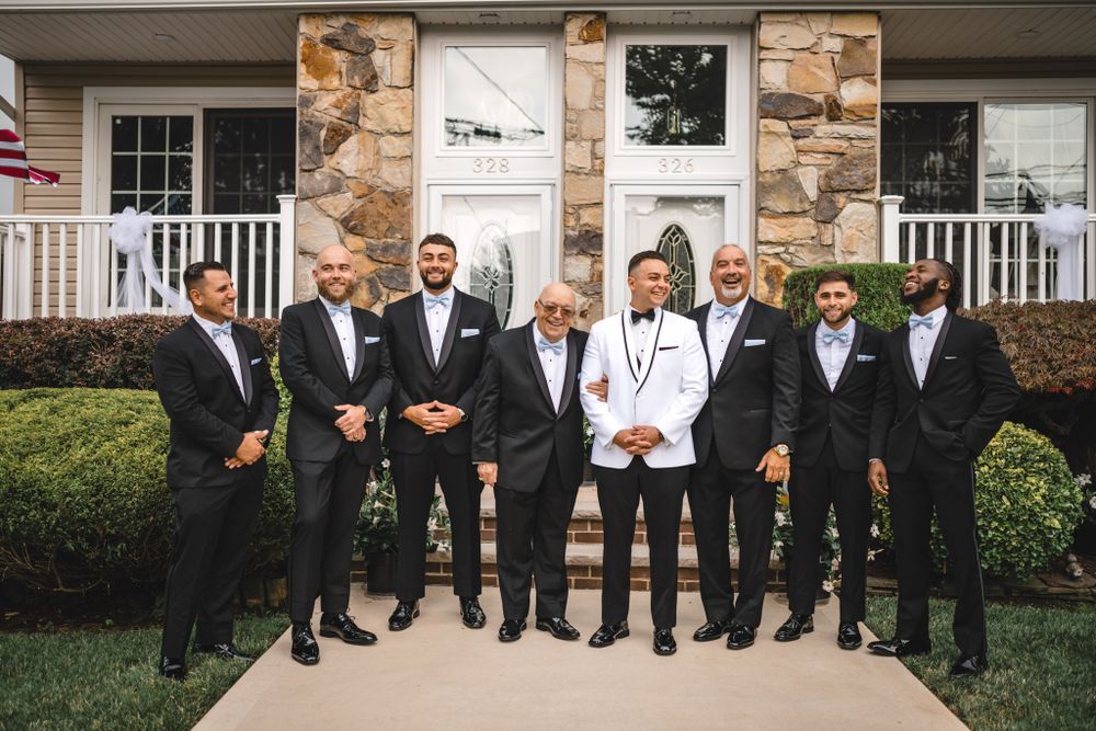 Wedding party in formal attire posing on stone steps outside a building.