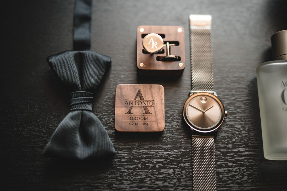 Wedding day accessories arranged on dark wood surface including bow tie and watch.
