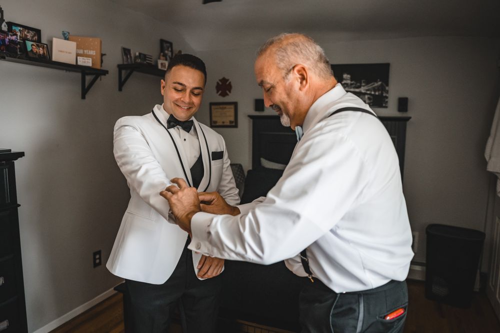 Black and white photo of two people helping with formal attire adjustments.