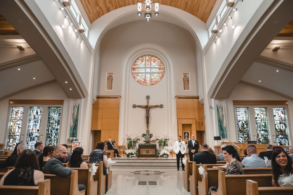 Wedding ceremony in a traditional church with vaulted wooden ceiling and stained glass windows.