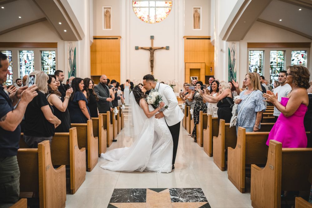 A black and white photo of a couple exiting through church doors as guests gather outside.