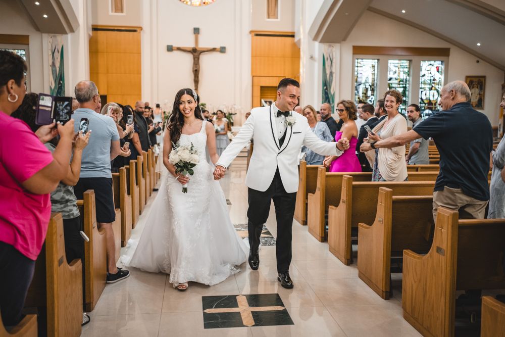 Newlyweds celebrate while walking down the church aisle as guests take photos from the pews.