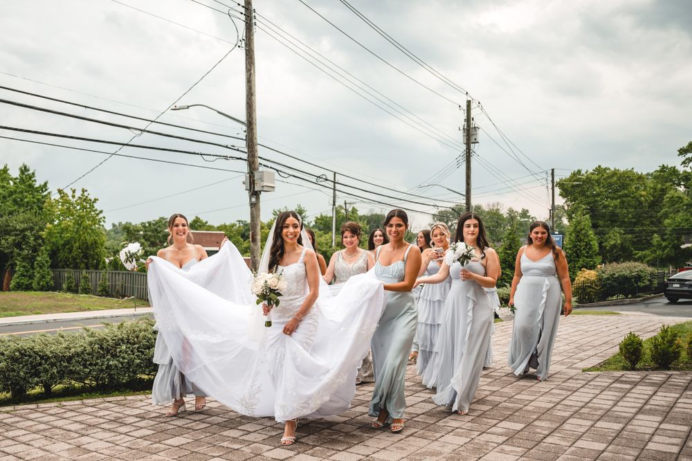 Wedding party in white and gray attire posing together outdoors on a cloudy day.