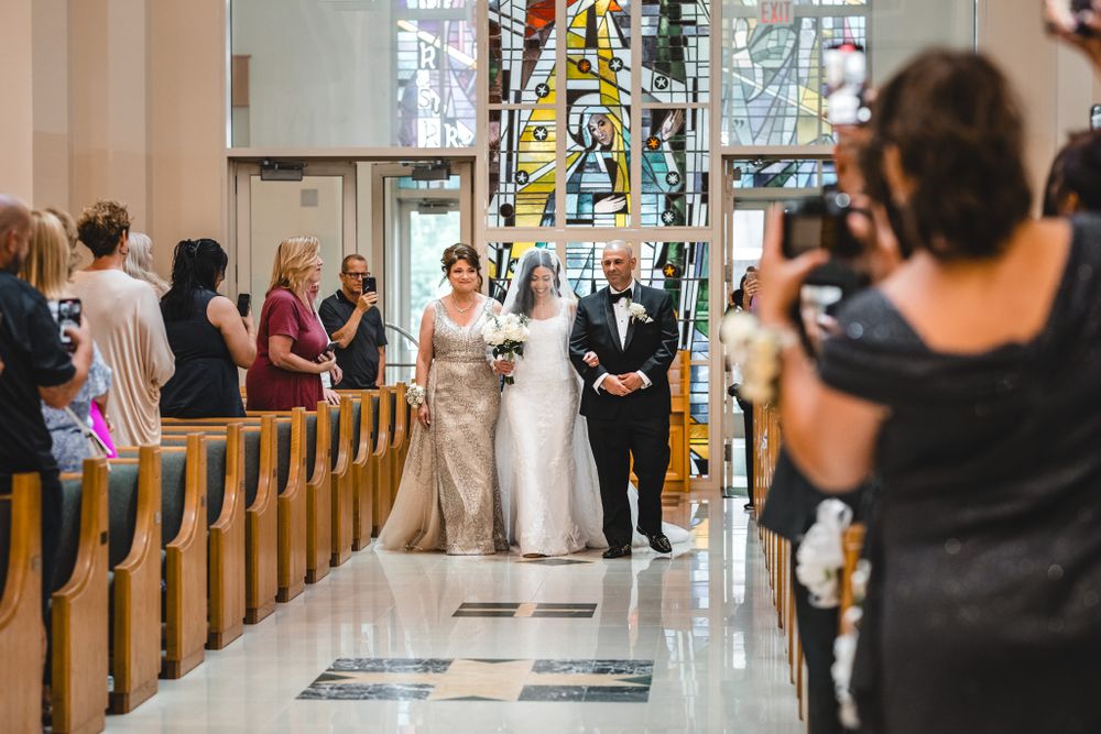 Wedding ceremony procession walking down church aisle with guests watching from pews.