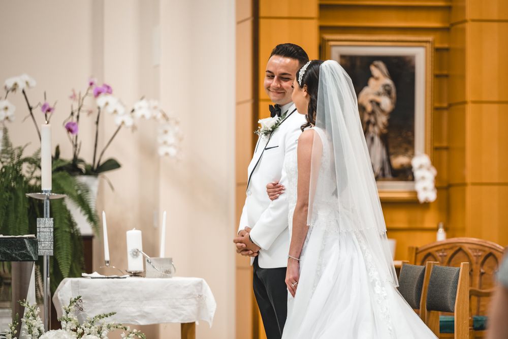 Wedding ceremony in progress inside church with floral decorations and natural lighting.