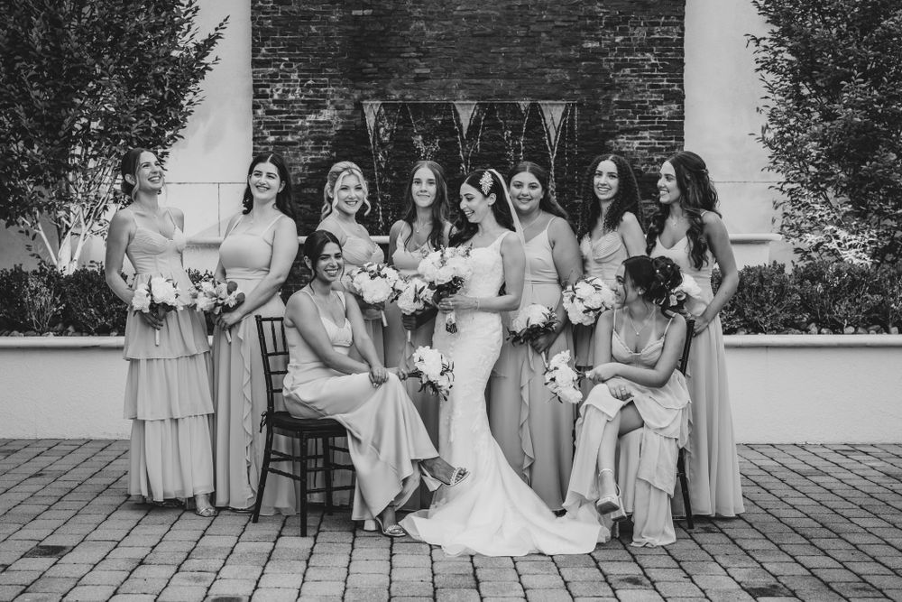 Wedding party group photo against stone wall backdrop with bridesmaids in light colored dresses.