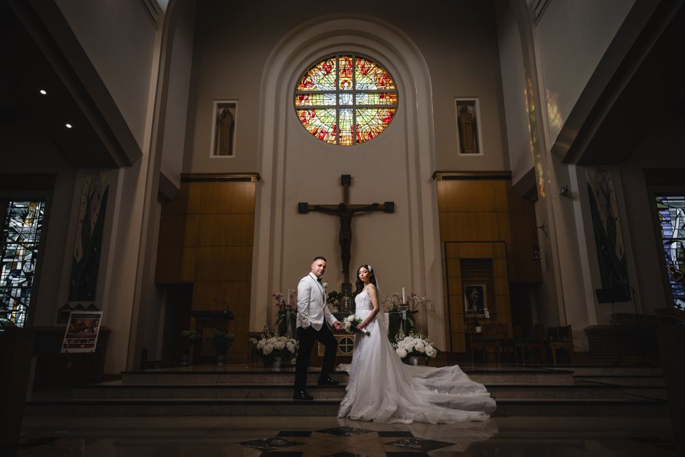 Dramatic church interior with stained glass windows and altar during wedding ceremony.
