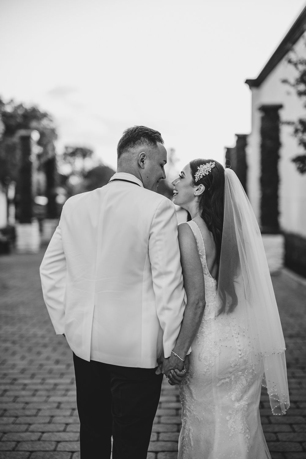 A black and white wedding photo series showing a couple walking together on a cobblestone path.