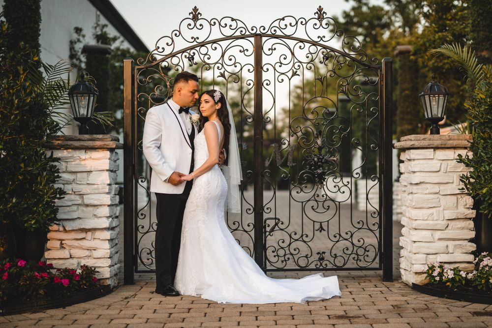 Wedding couple poses in front of elegant stone pillars and decorative iron gates.