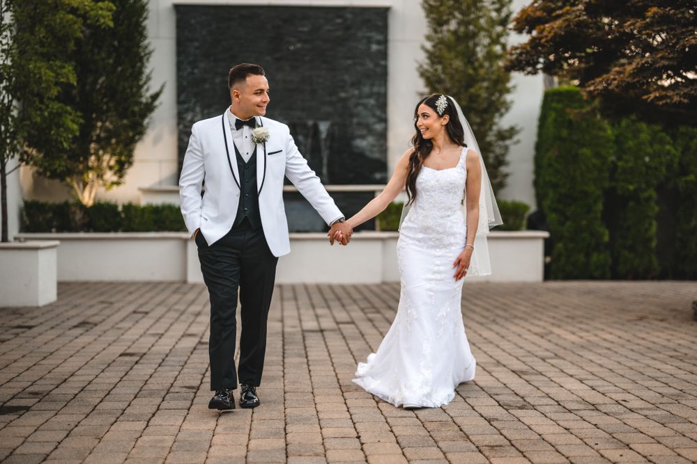 Wedding couple poses on brick patio surrounded by greenery and architecture.