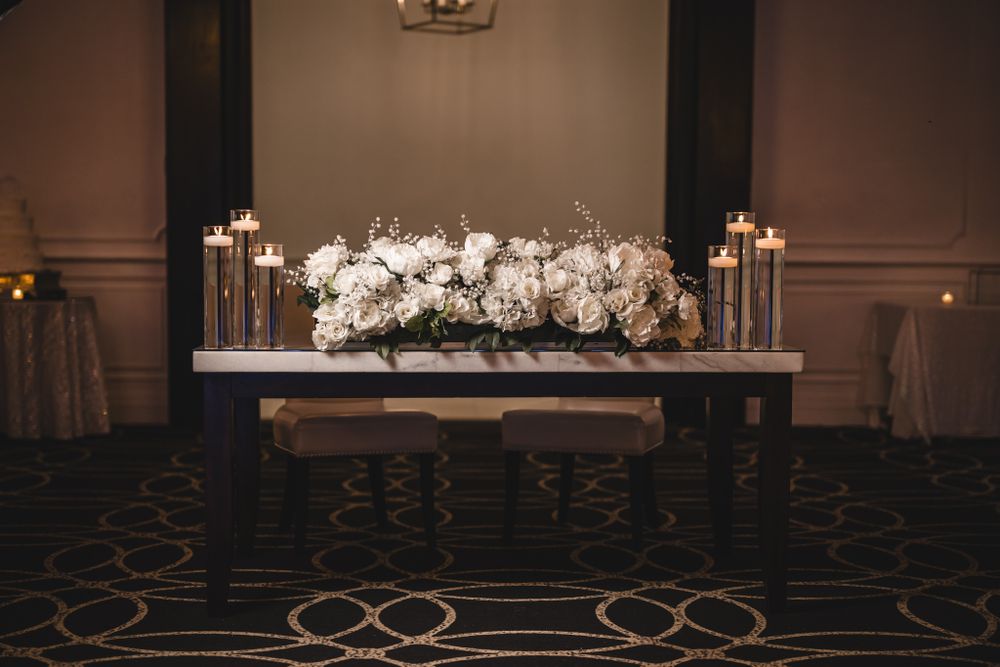 Elegant wedding reception hall setup with white floral arrangements and chandeliers.