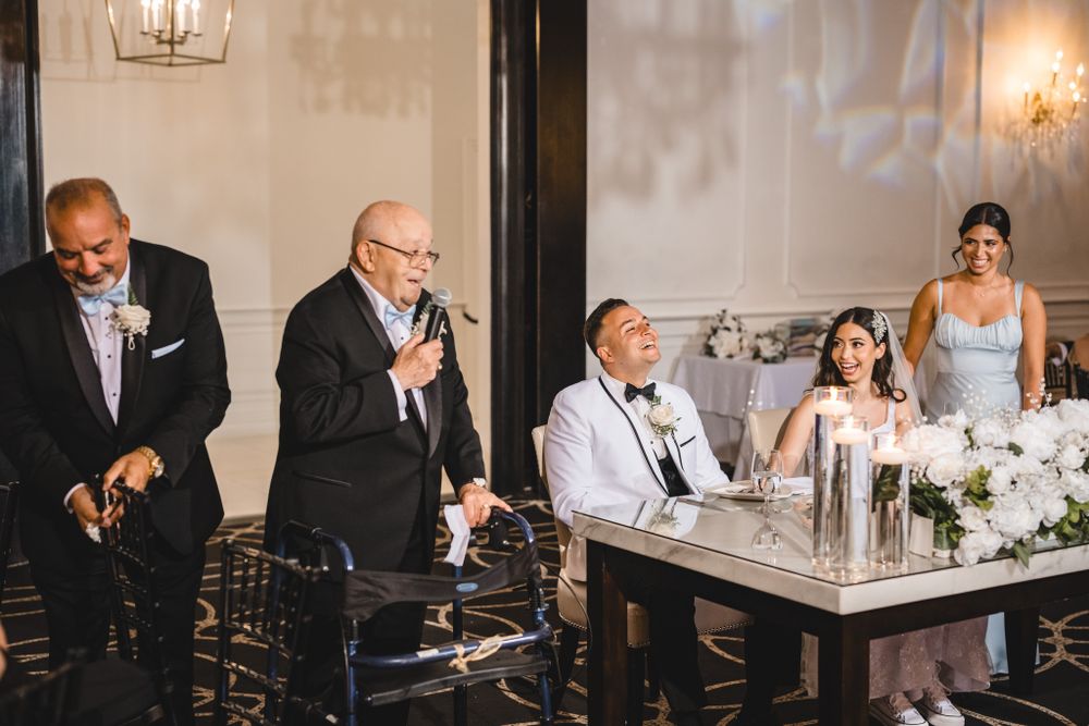 Wedding toasts being given at reception head table with elegant white floral centerpieces.