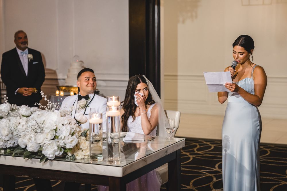 Wedding reception speeches at elegant head table decorated with white flowers and candles.