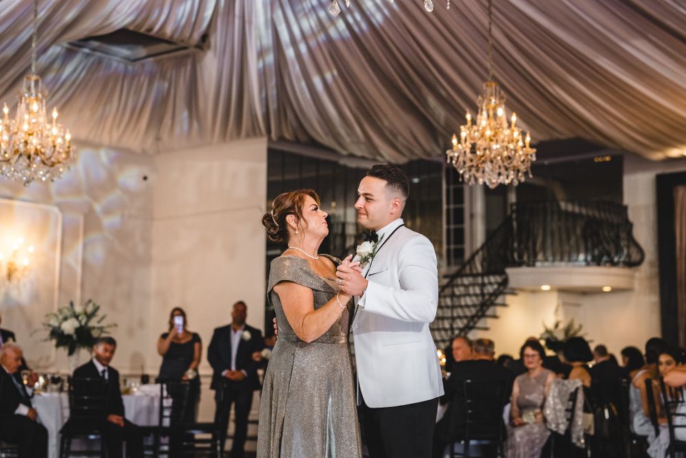 Wedding reception guests dancing and celebrating under elegant chandeliers in a draped ceiling venue.