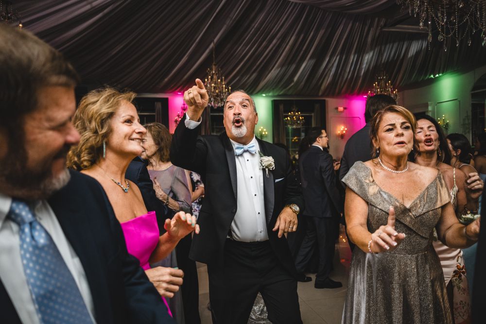 Lively dance party at an elegant wedding reception with colorful lighting and draped decor.