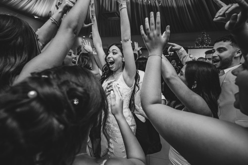 Black and white photo of energetic wedding reception dancing with hands raised in celebration.