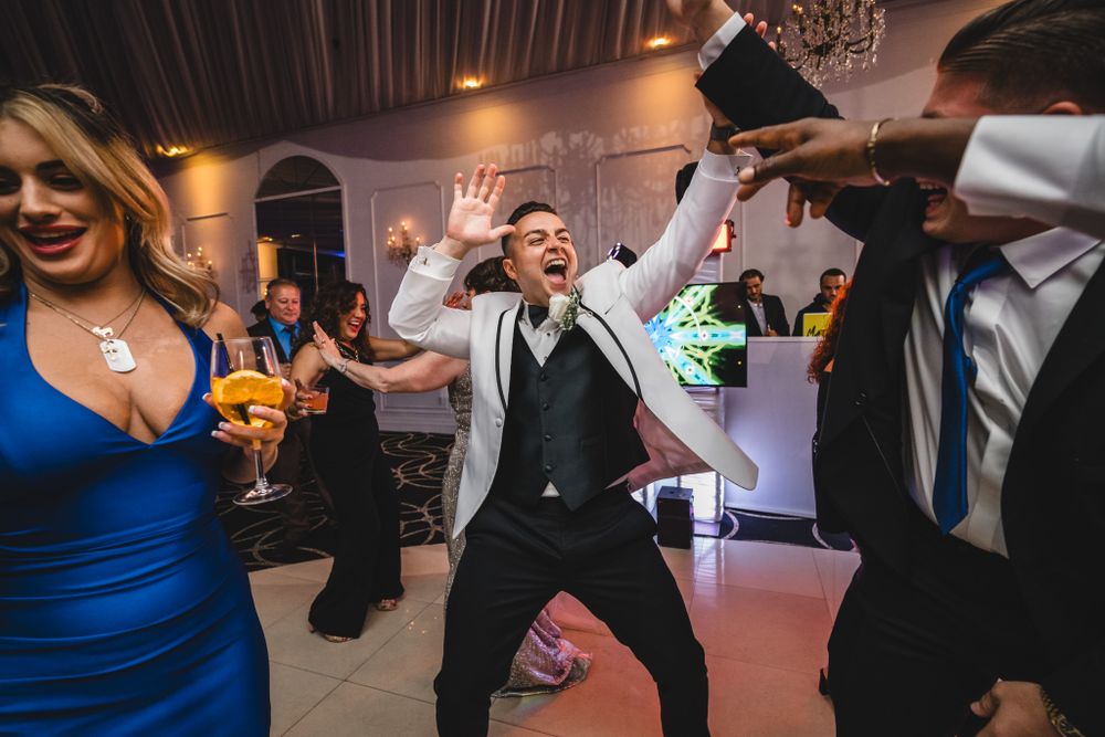 Wedding guests dancing enthusiastically at reception with dramatic lighting and decor.