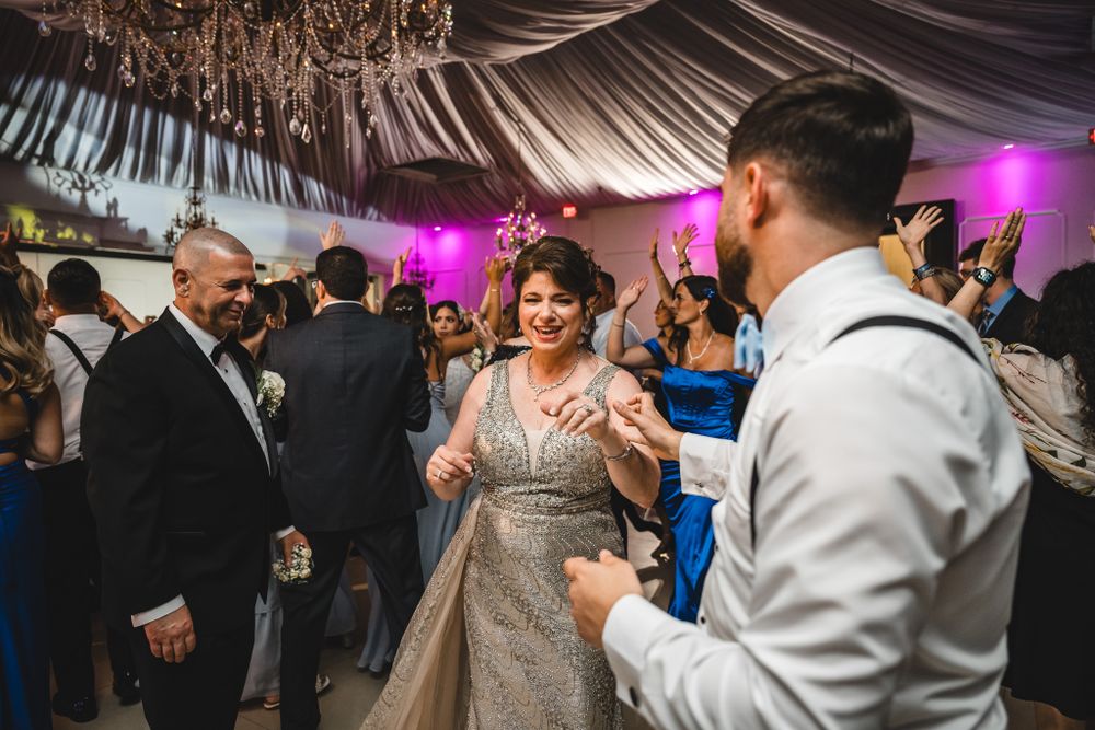 Wedding party dancing and celebrating under elegant draped ceiling with purple accent lighting.