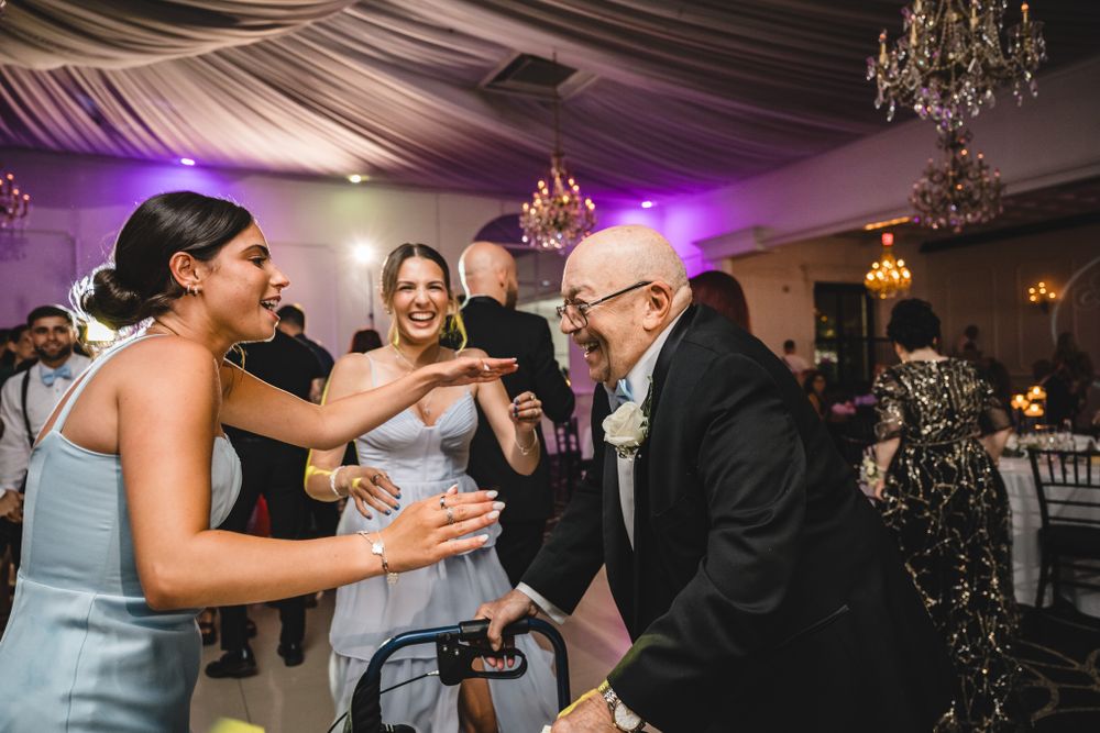 Wedding guests enjoying dance floor moments under crystal chandeliers and draped ceiling.