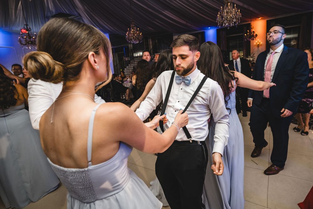 Wedding reception guests dancing in formal attire under elegant venue lighting.