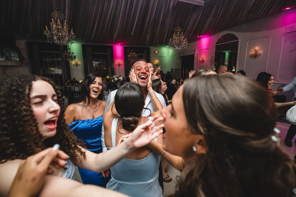 Candid moments of joyful celebration on wedding reception dance floor with pink lighting.