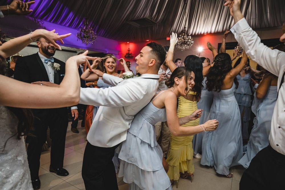 Wedding guests dance enthusiastically on a colorfully lit dance floor during an evening reception celebration.