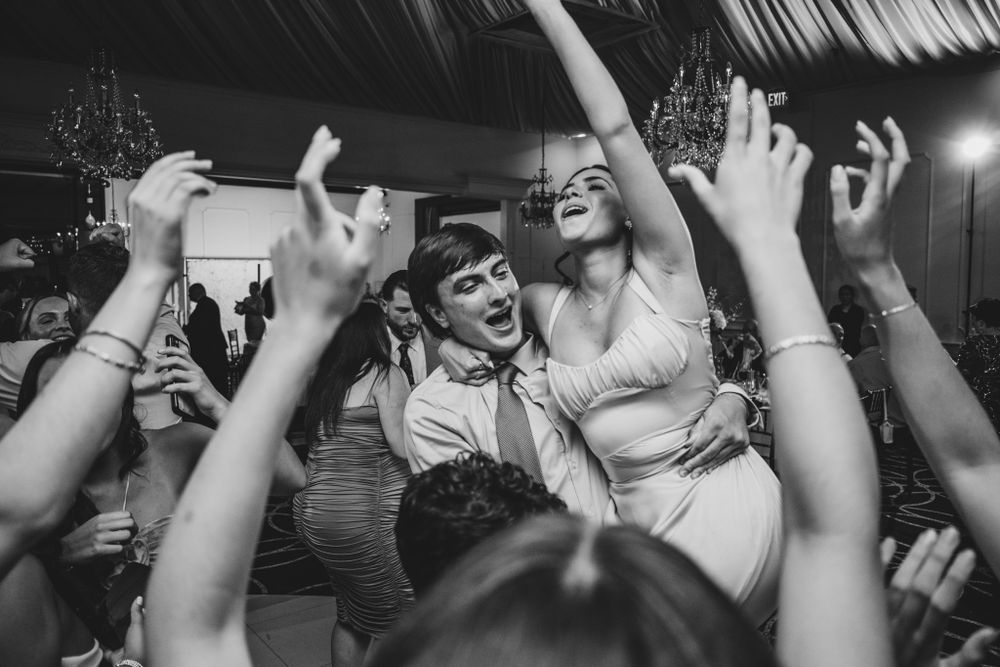 Joyful wedding party dancing and celebrating with hands raised under purple and red lighting.