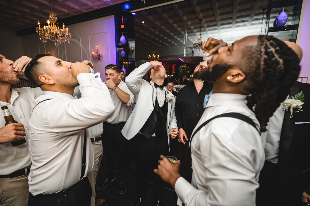 Wedding reception guests dancing energetically in a dimly lit venue with chandeliers overhead.