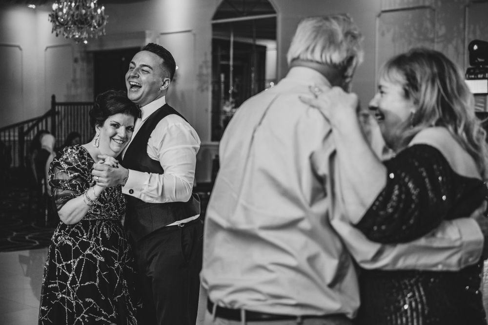Black and white photo of wedding guests embracing and dancing during an indoor reception.