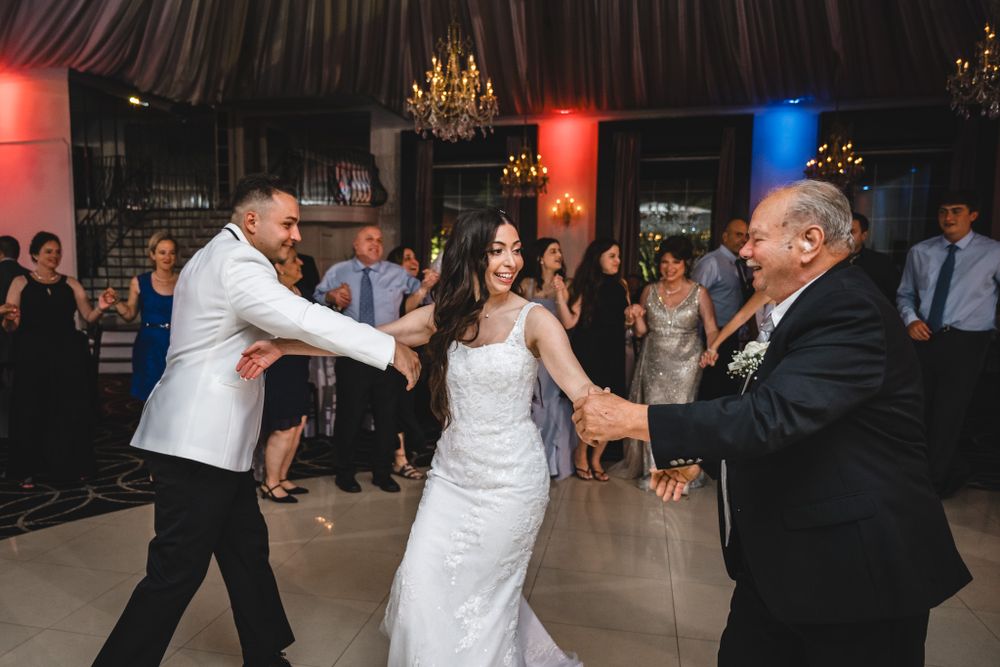 Wedding reception venue decorated with elegant chandeliers and colored lighting as guests dance.