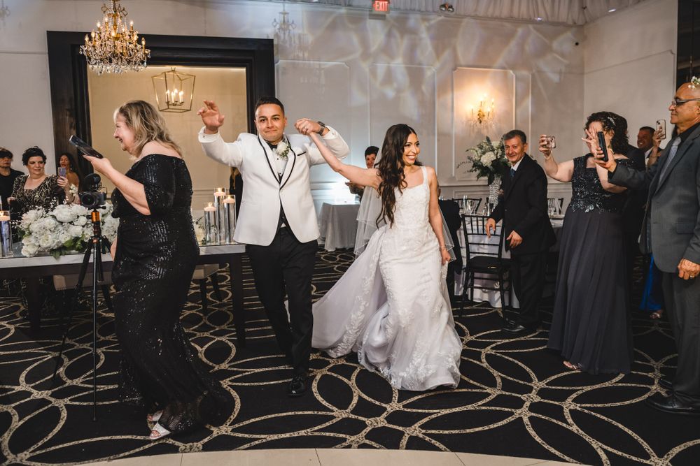 Wedding guests dancing and celebrating on an elegant ballroom floor with chandeliers and decorative carpet patterns.