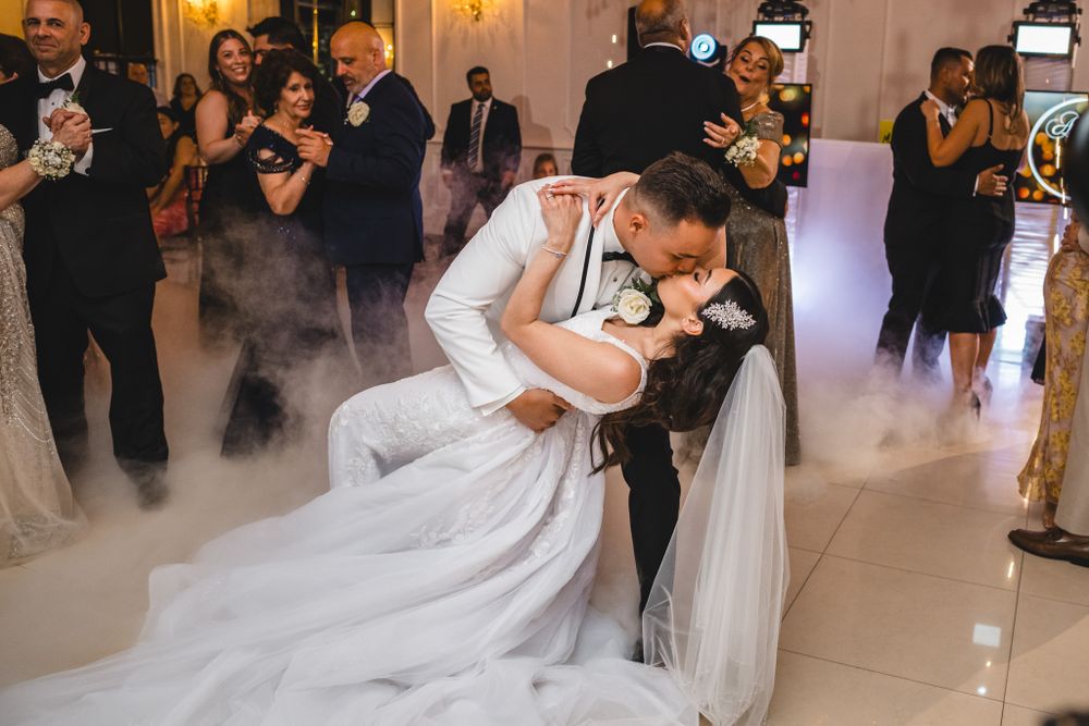 Romantic dip during wedding dance with flowing white dress and dramatic fog effect on ballroom floor.