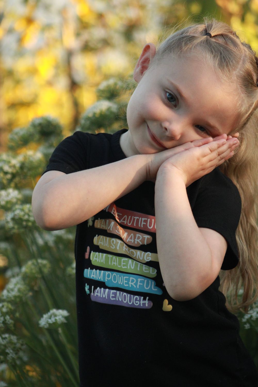 Posing in a black t-shirt with colorful text against a sunny yellow garden backdrop.