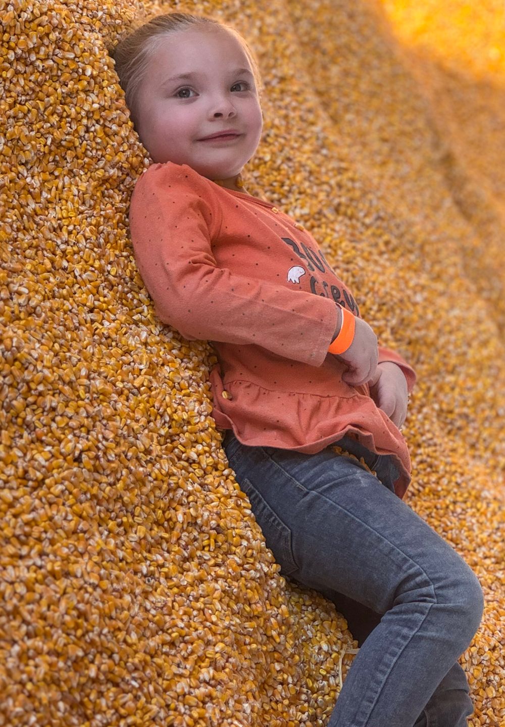 Casual pose against golden corn pile wearing coral colored shirt.