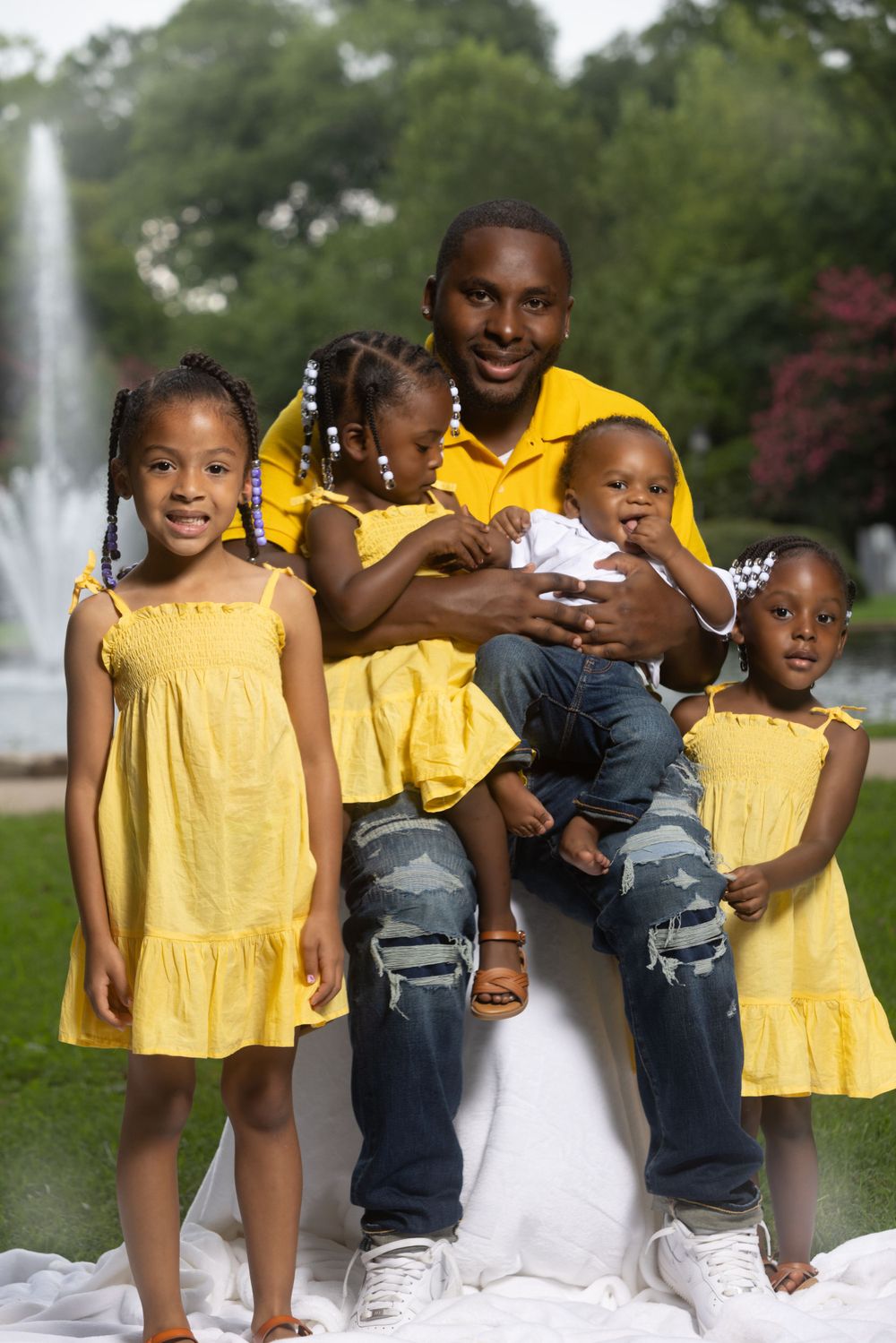 Family portrait with children in matching yellow dresses by fountain in park setting.