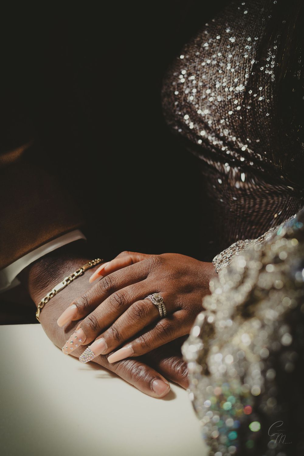 Detail shot of hands with rings and sparkling formal attire in moody lighting.