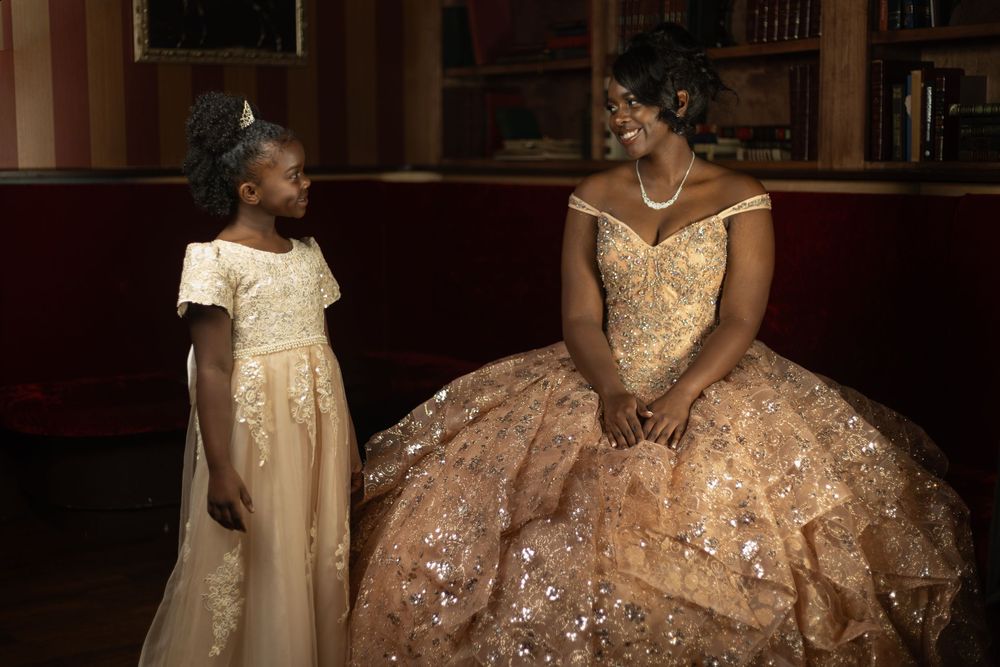 A group of elegant ballgowns in champagne and gold tones displayed in a dimly lit formal setting.