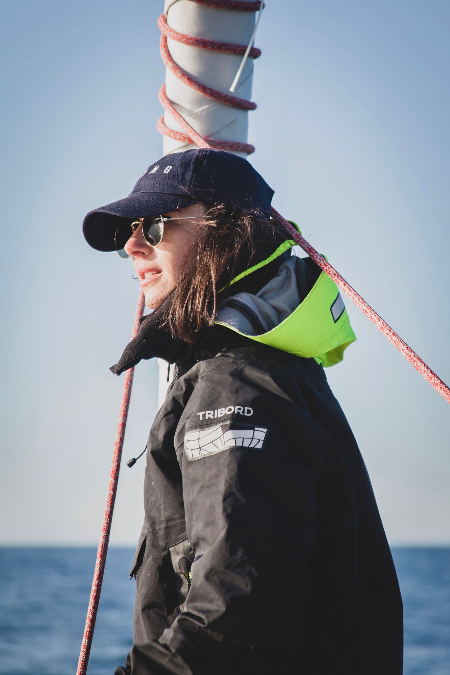 Portrait d’une navigatrice en mer, vêtu d’une veste technique et d’une casquette.