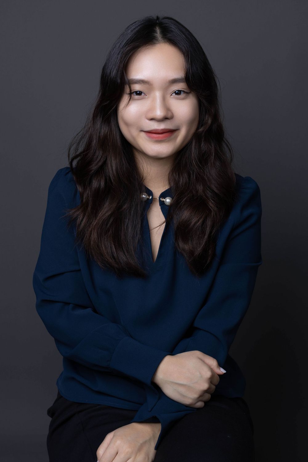 Young Asian woman in navy blouse smiling warmly in an elegant studio portrait.