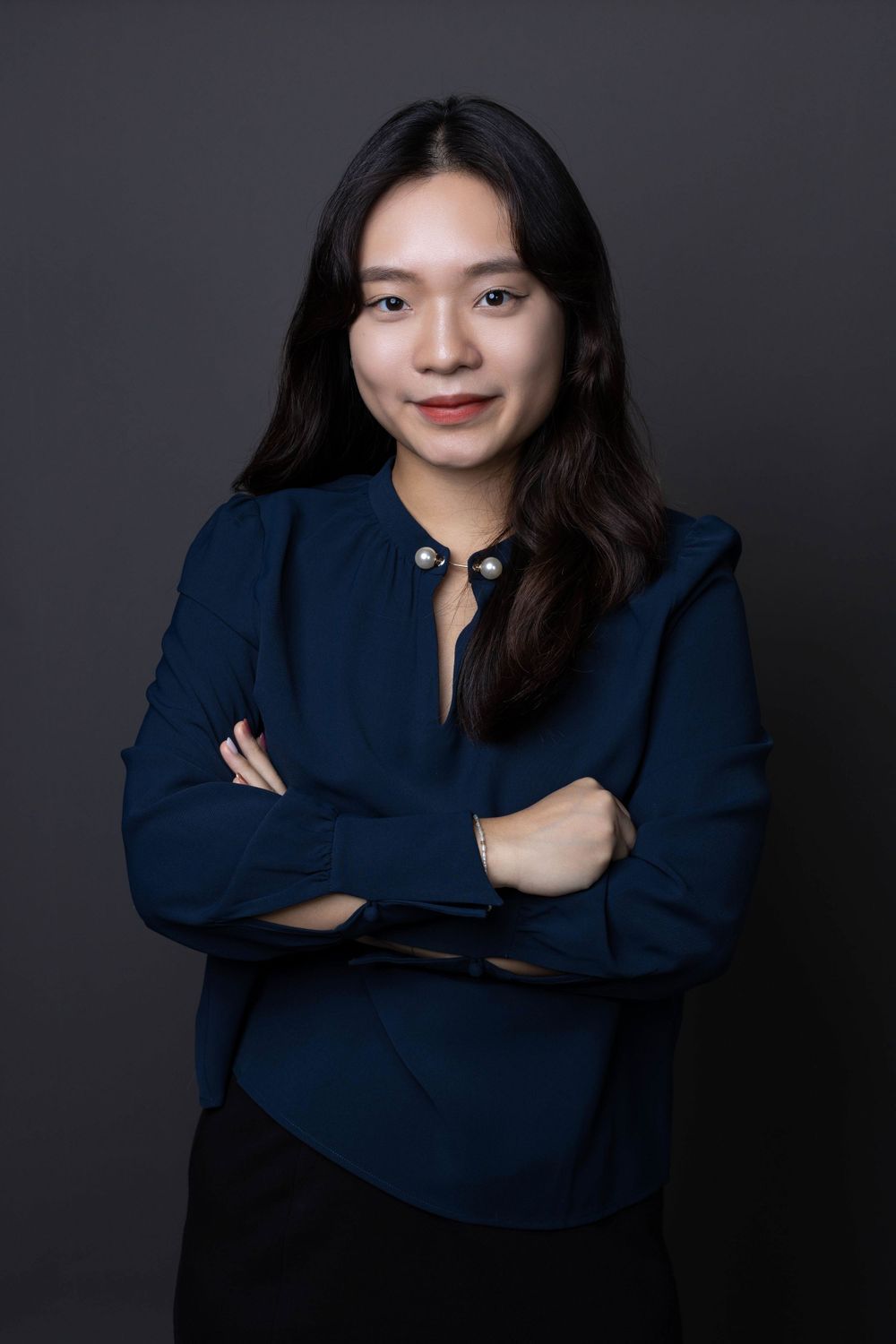 Smiling Asian woman in navy blue blouse posing with arms crossed in professional studio portrait.