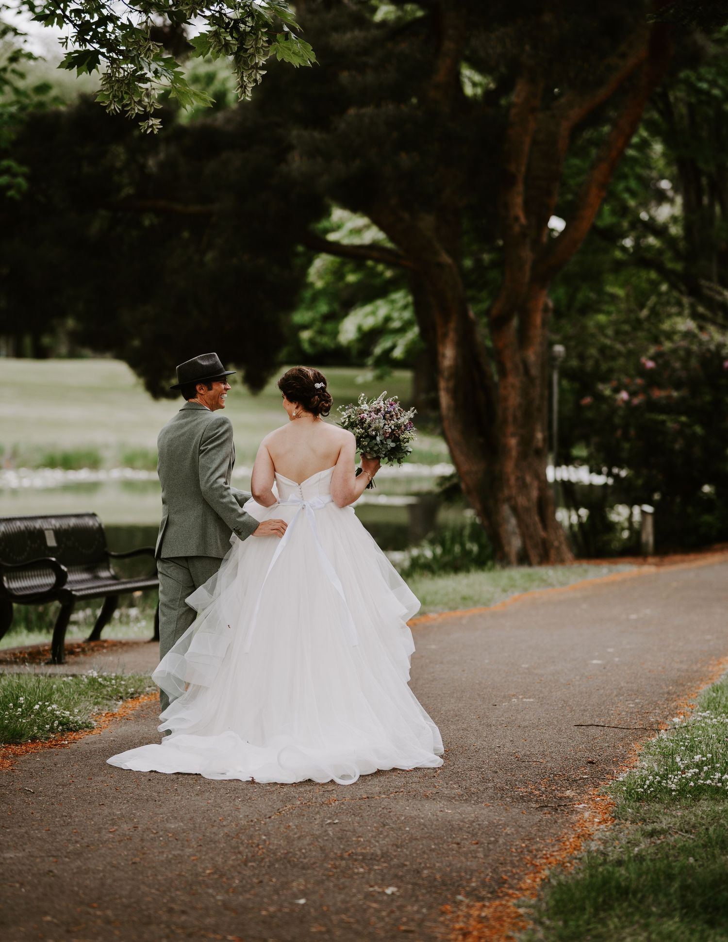 Newlyweds share an intimate moment on a tree-lined path in a park.