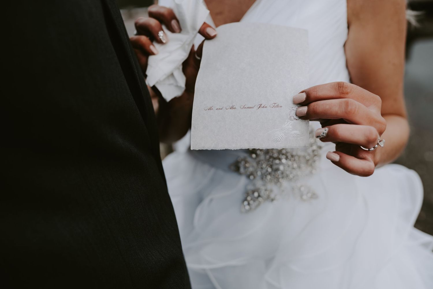 Hands holding handwritten wedding vows on white paper against a flowing wedding dress.