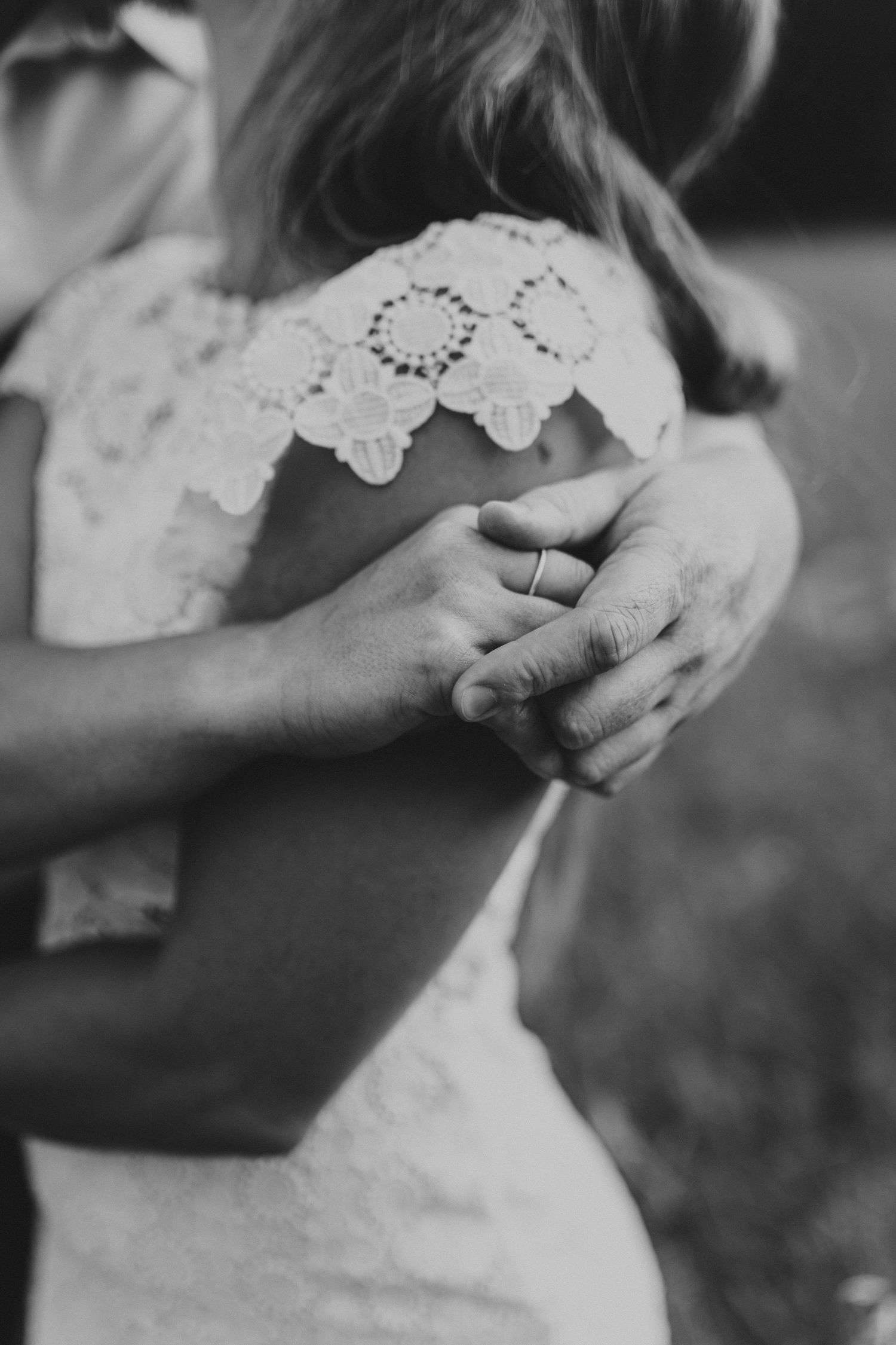 Black and white detail shot of hands with lace dress sleeve and engagement ring.