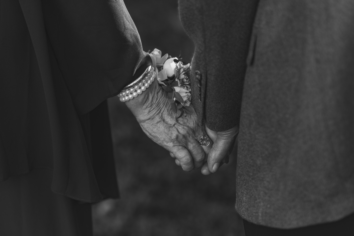 Black and white photo of two people holding hands with floral corsages.