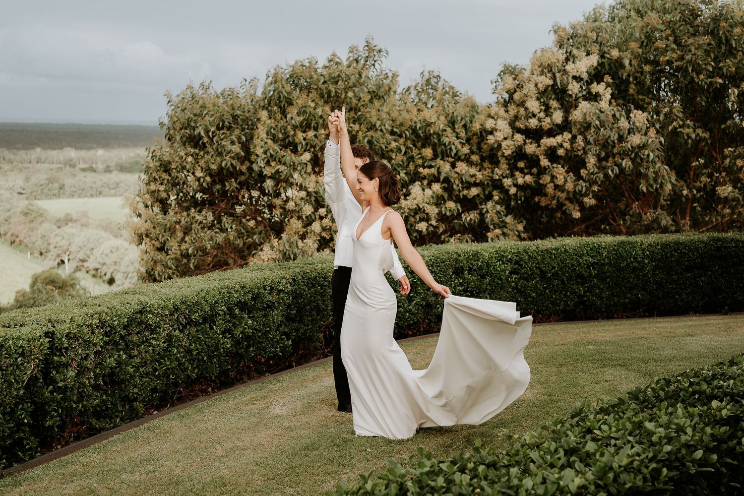 A bride in a flowing white dress walks through a lush green garden path at Yeppoon wedding venue on a sunny afternoon.