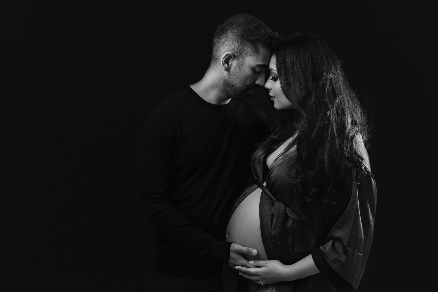 Expecting parents in a loving embrace with expecting fathers hand cradling baby bump