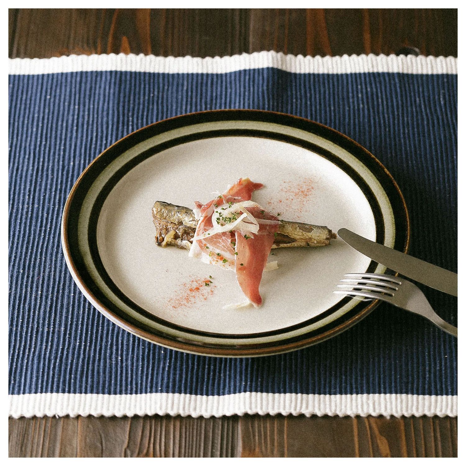 A series of white plates with remnants of eaten food on a dark wooden table with blue placemats.
