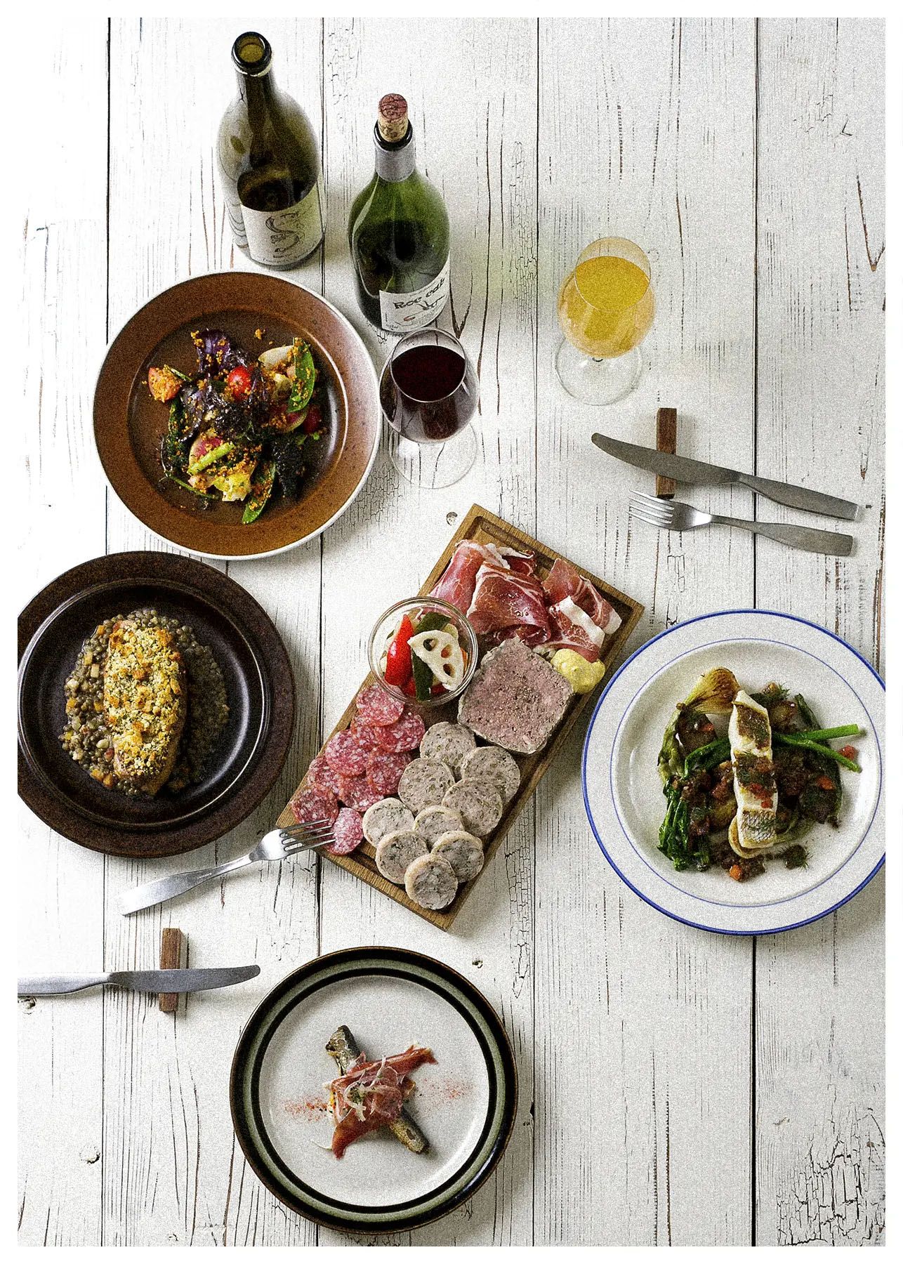 Overhead view of multiple elegant dinner plates with meat dishes and sides on a rustic white wooden table.