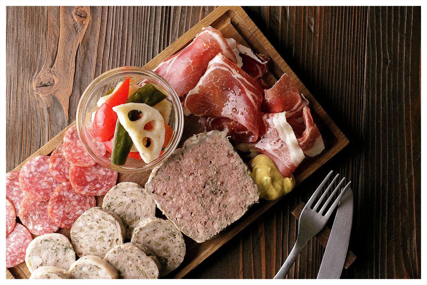 Various cuts of raw meat and charcuterie arranged on a rustic wooden serving board.